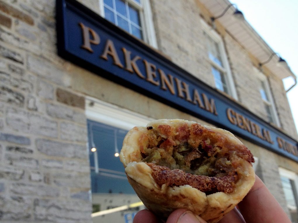 hand holding a butter tart in front of a store sign