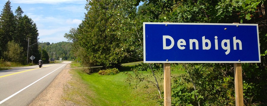 Motorcycle riding on road past Denbigh sign